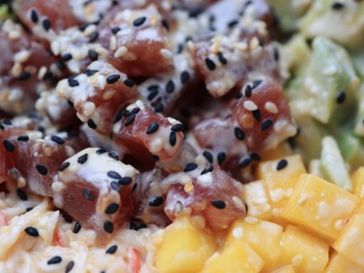 A vibrant poke bowl featuring ahi tuna, mango, avocado, and black sesame seeds.