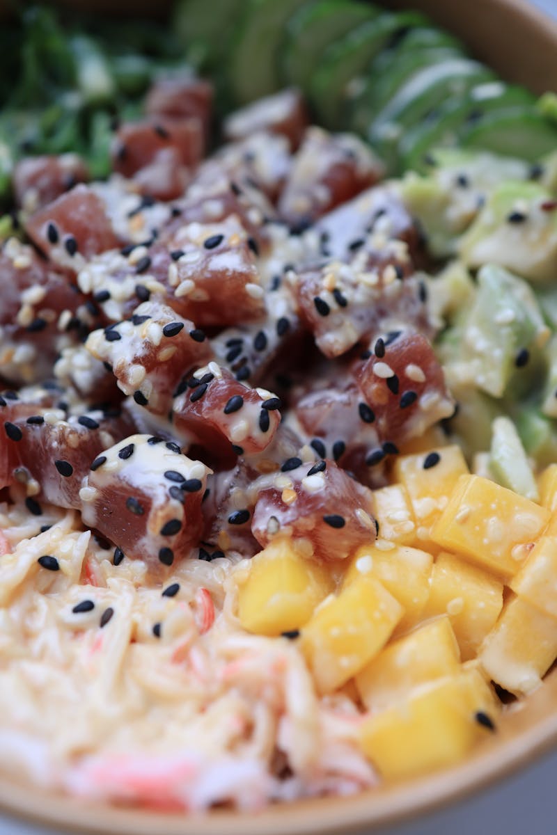 A vibrant poke bowl featuring ahi tuna, mango, avocado, and black sesame seeds.