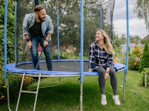 Smiling couple bonding on a trampoline surrounded by greenery and flowers.
