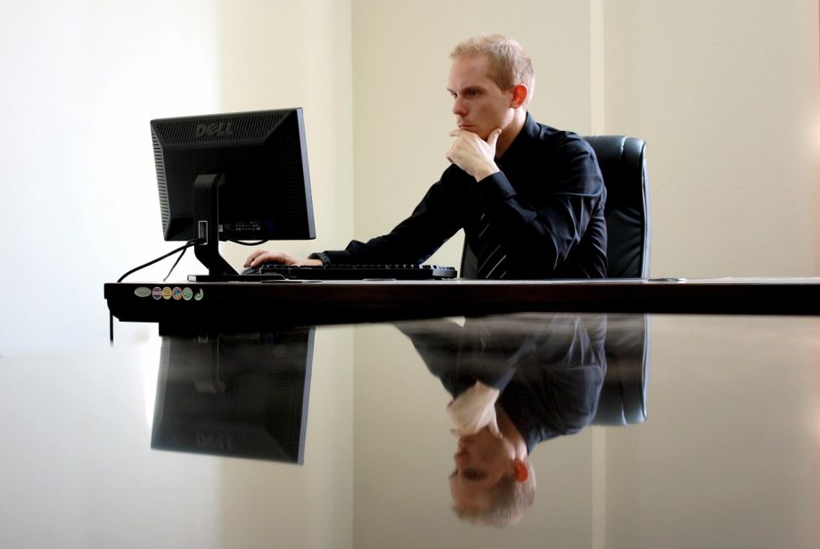 Man achter een opgeruimd bureau met laptopstandaard, toetsenbord en andere bureau gadgets